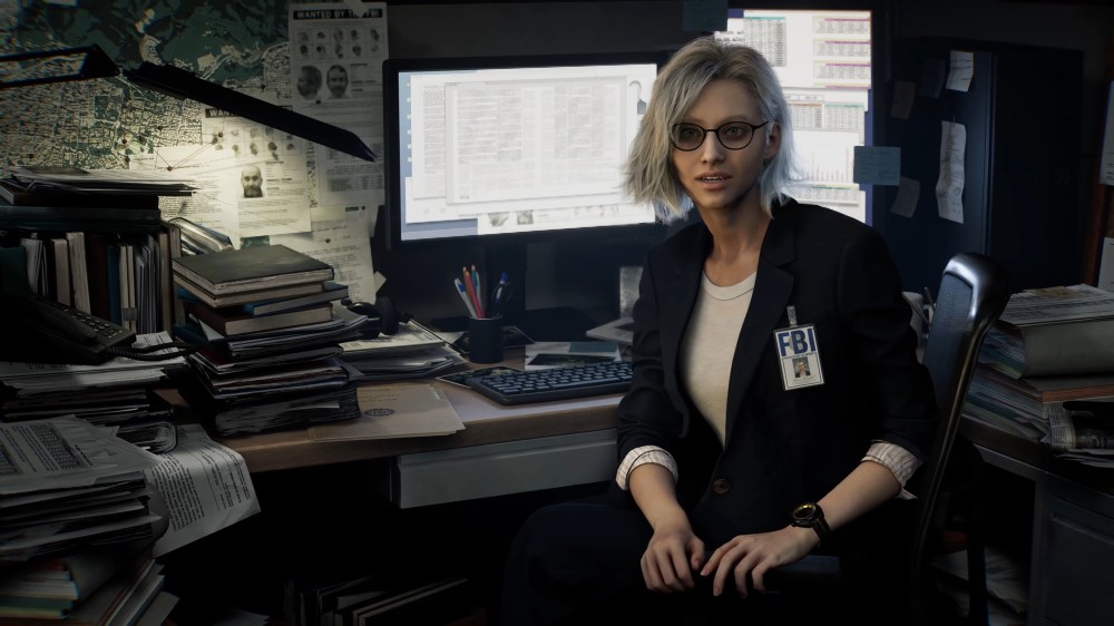 A female character with blonde hair and glasses, dressed in a black suit with an FBI badge, sits at a cluttered desk filled with stacks of papers and documents, looking at the camera with a slight smile.