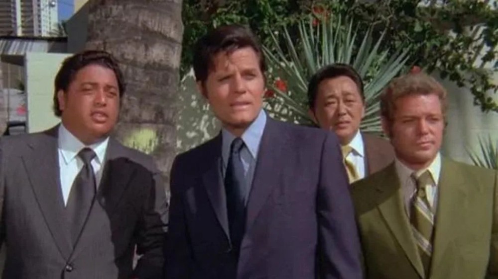 Four men in business suits standing outdoors with palm trees in the background.