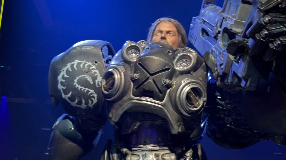 A detailed robot figure with a human-like face, wearing heavy armor and holding a large weapon. The armor features a unique logo and has intricate mechanical details.
