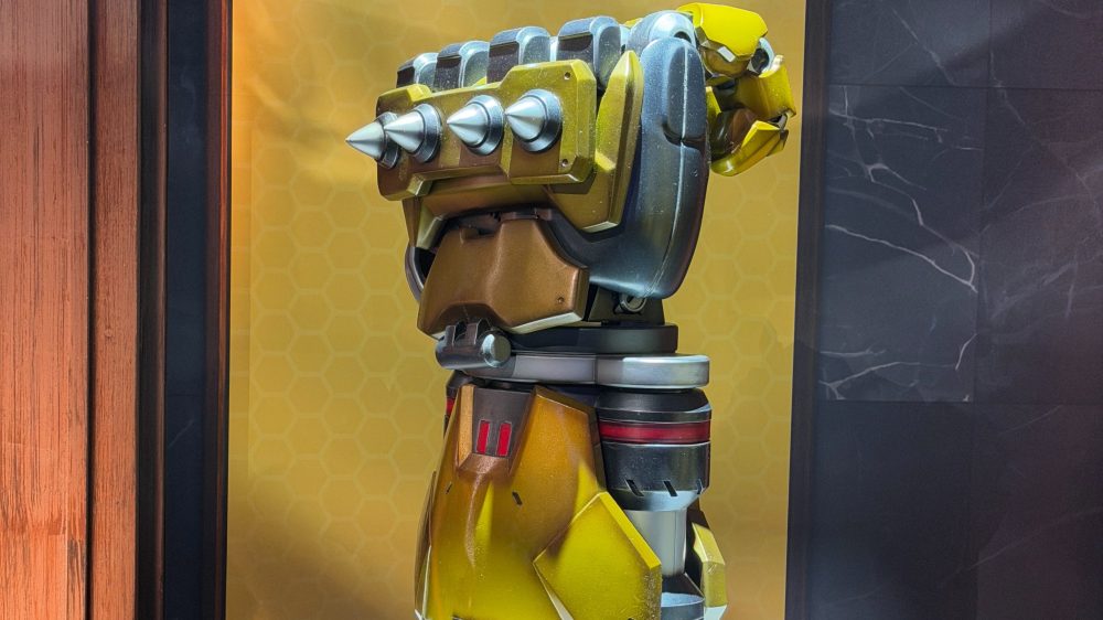A side view of a robotic arm with a yellow and metallic design, featuring spikes on the shoulder and a flexible joint.