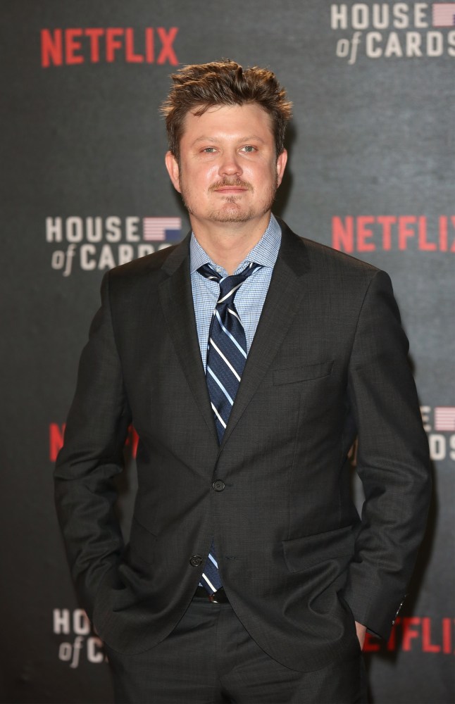 A man in a gray suit stands in front of a promotional backdrop for Netflix's 'House of Cards,' with the Netflix logo prominently displayed.