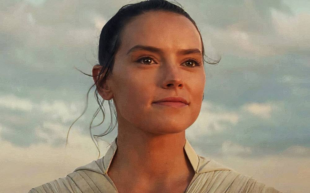 Close-up portrait of a woman with long hair, wearing a light-colored garment, looking confidently towards the horizon with a cloudy sky in the background.