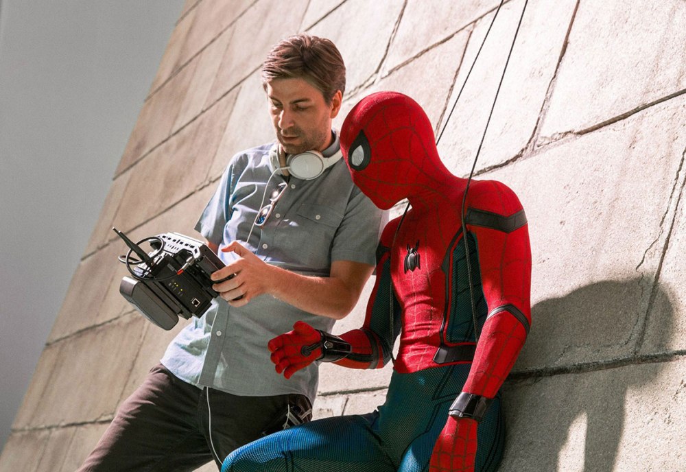 A film crew member reviewing footage on a monitor while sitting next to a Spider-Man figure on a wall.