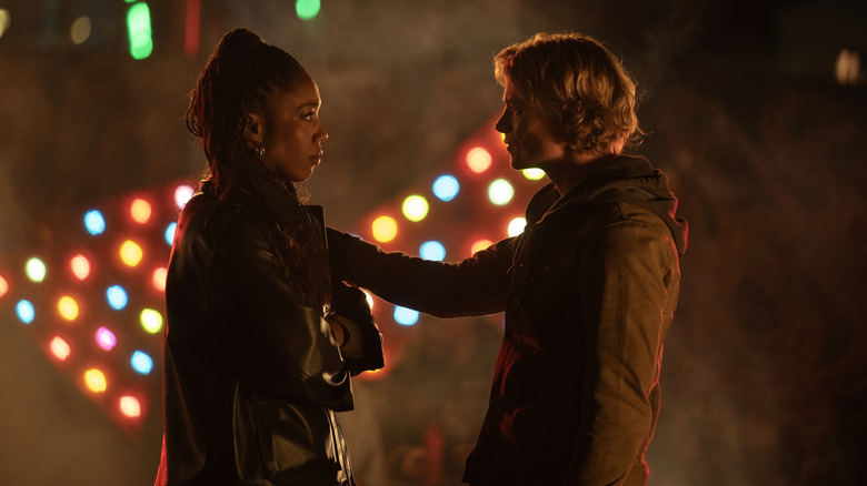 A dramatic scene featuring two people facing each other with intense expressions, illuminated by colorful lights in the background.