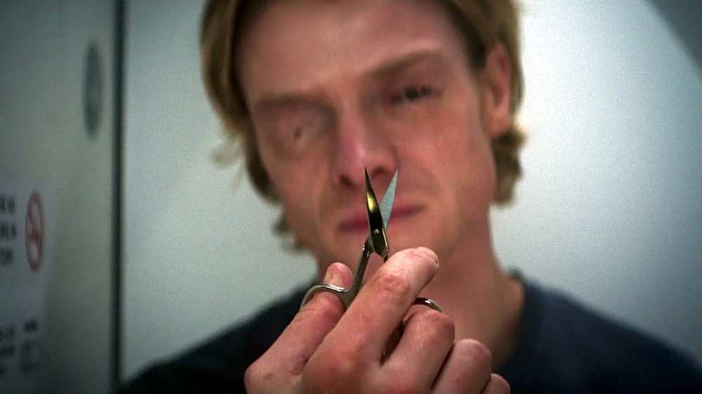 A close-up of a young man holding a pair of scissors, staring intently ahead with a serious expression.